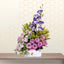 Bouquet of pink and purple flowers in a white box on a wooden surface with a geometric patterned wall in the background.