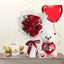 Small bouquet of three red roses in white wrapping, next to a white teddy bear, a box of chocolates, and a red heart balloon.