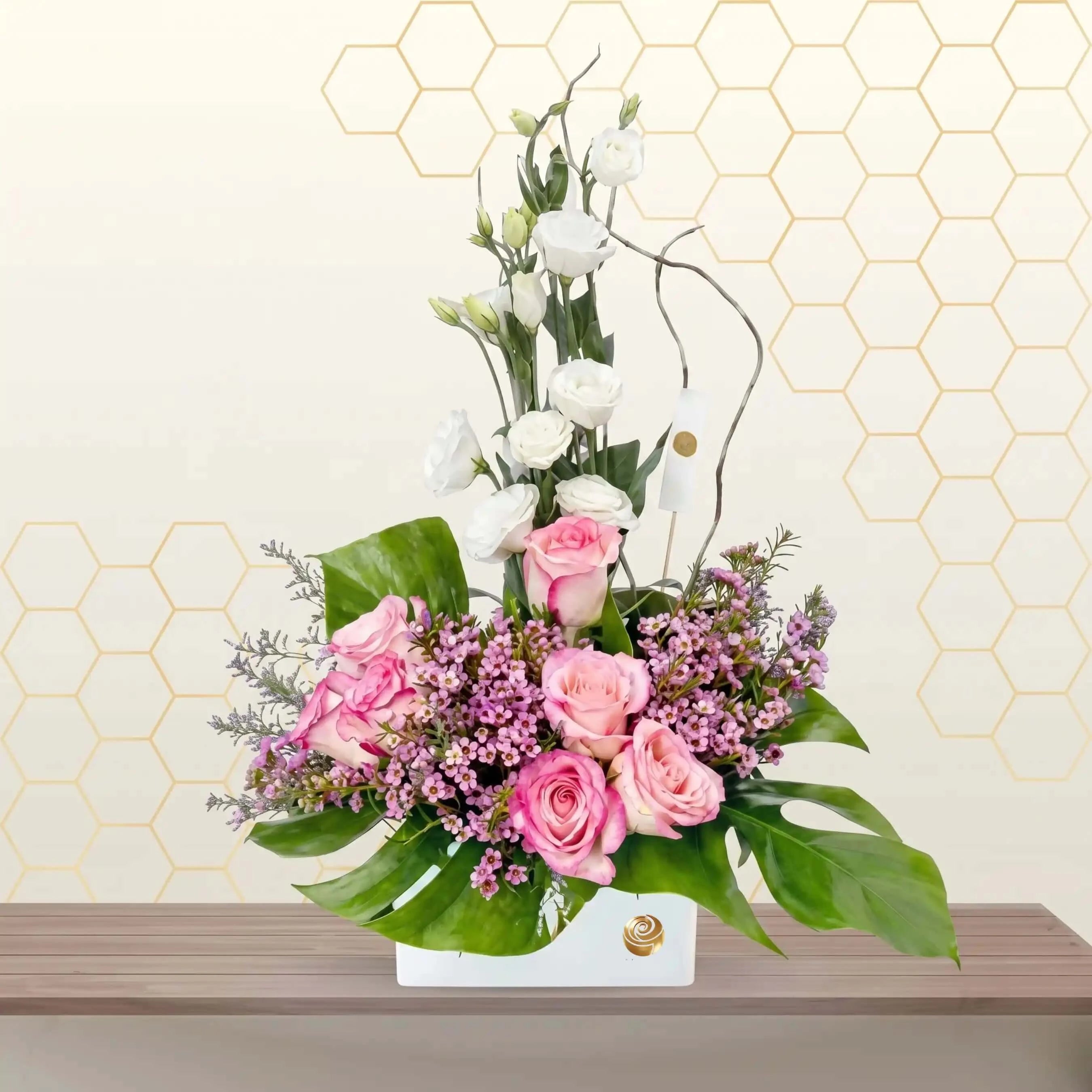Floral arrangement with pink and white flowers on a wooden surface against a geometric patterned wall.