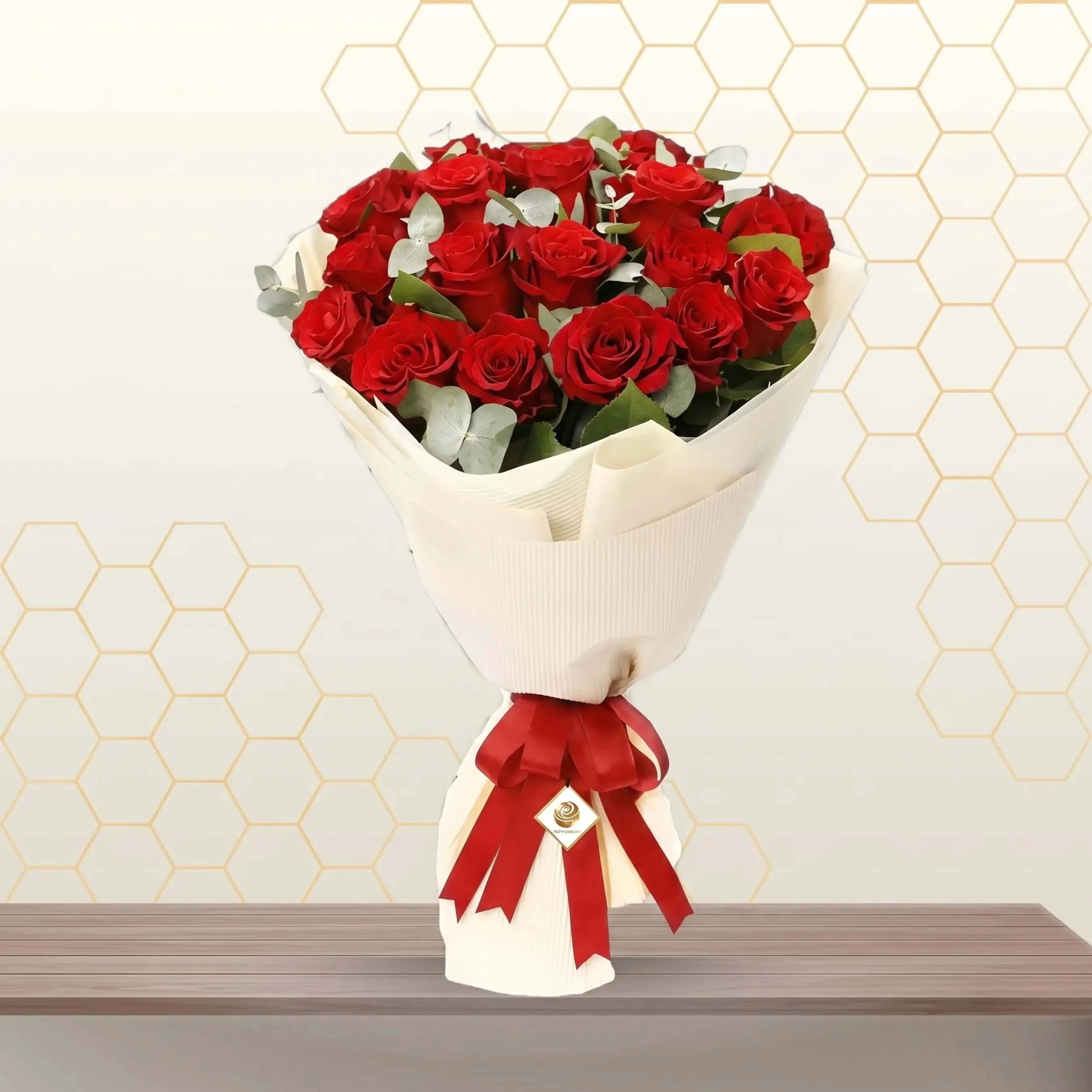 Bouquet of red roses wrapped in white paper with a red ribbon on a hexagonal patterned wall.