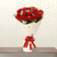 Bouquet of red roses wrapped in white paper with a red ribbon on a hexagonal patterned wall.
