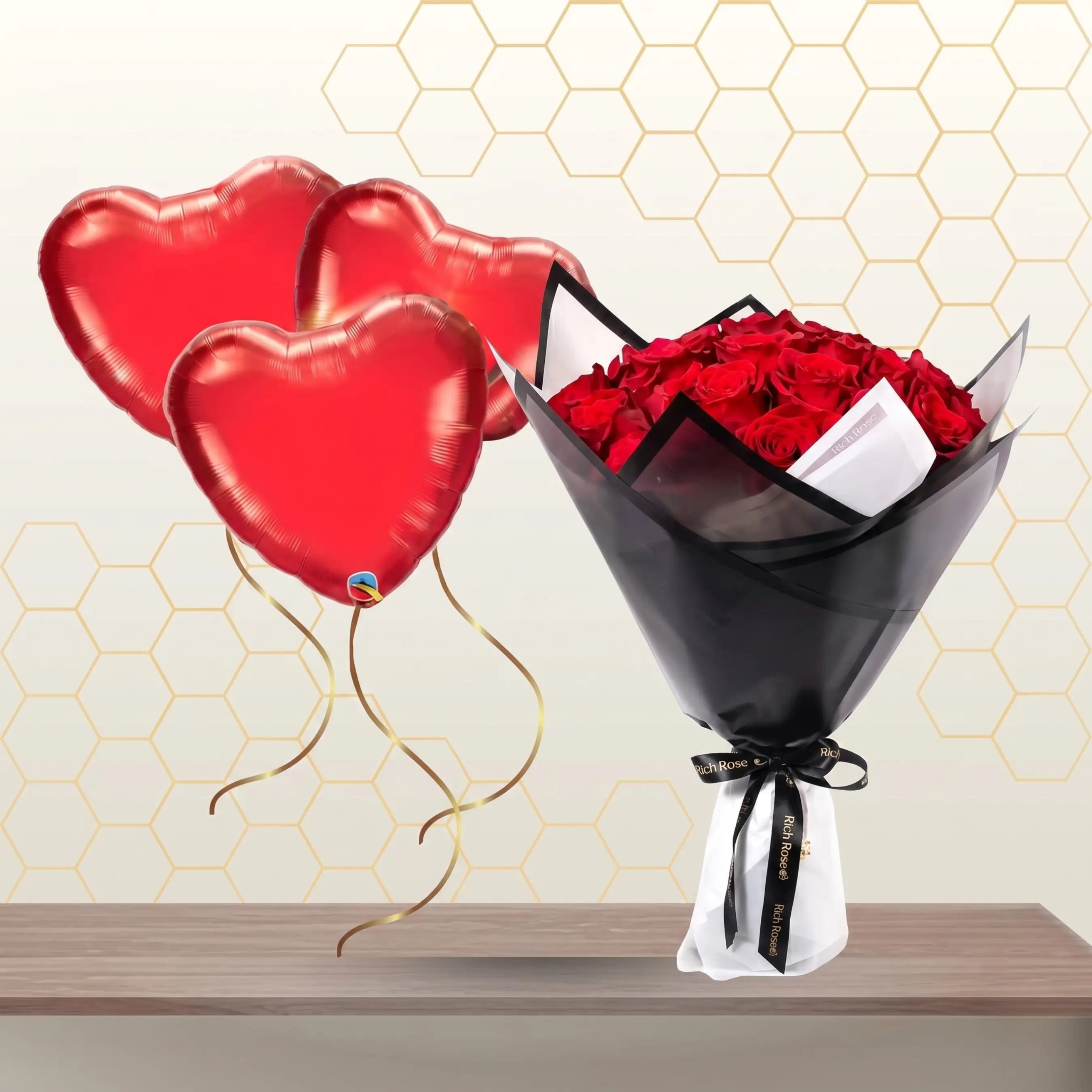 Bouquet of red roses wrapped in black paper with white lining, floating with three red heart-shaped foil balloons.
