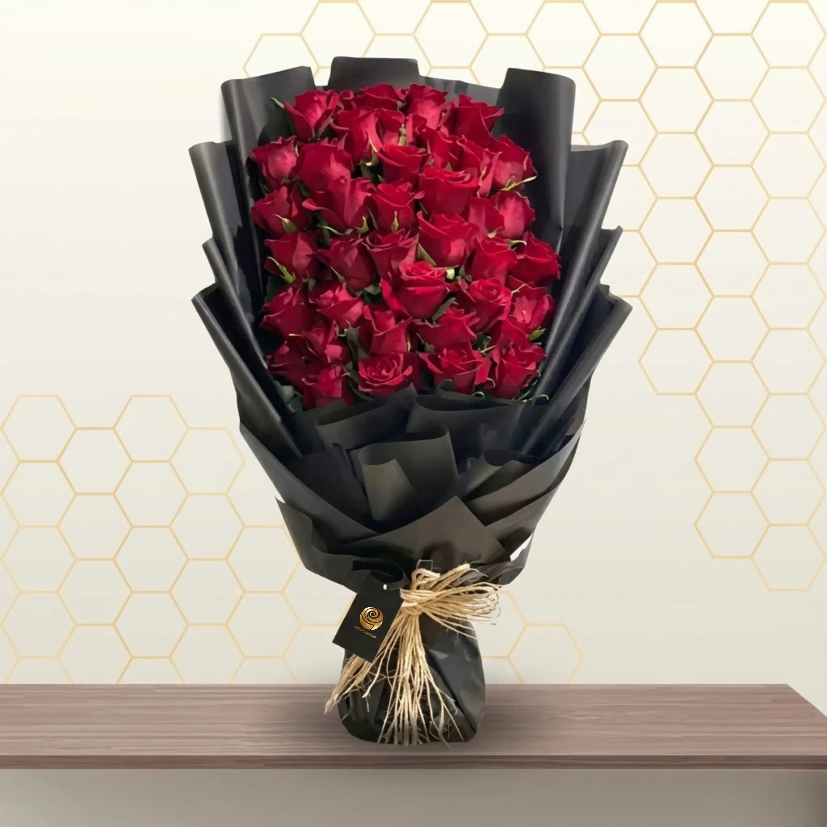 CHOCOLAT luxury heart-shaped bouquet of 27 red roses wrapped in premium matte black paper on a wooden table.