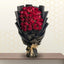 CHOCOLAT luxury heart-shaped bouquet of 27 red roses wrapped in premium matte black paper on a wooden table.