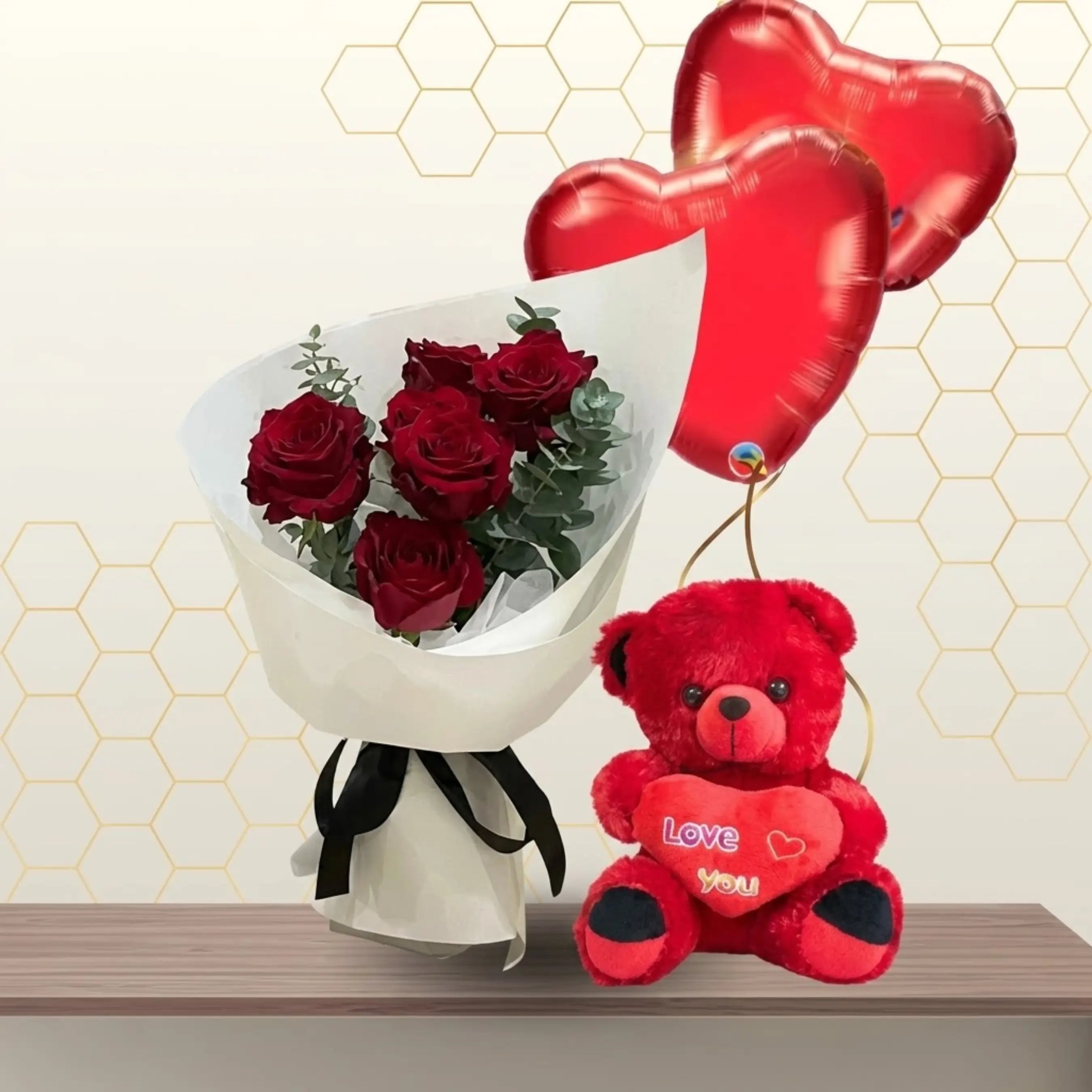 Bouquet of red roses in white paper next to a 45cm red teddy bear and two red heart balloons.