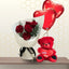 Bouquet of red roses in white paper next to a 45cm red teddy bear and two red heart balloons.