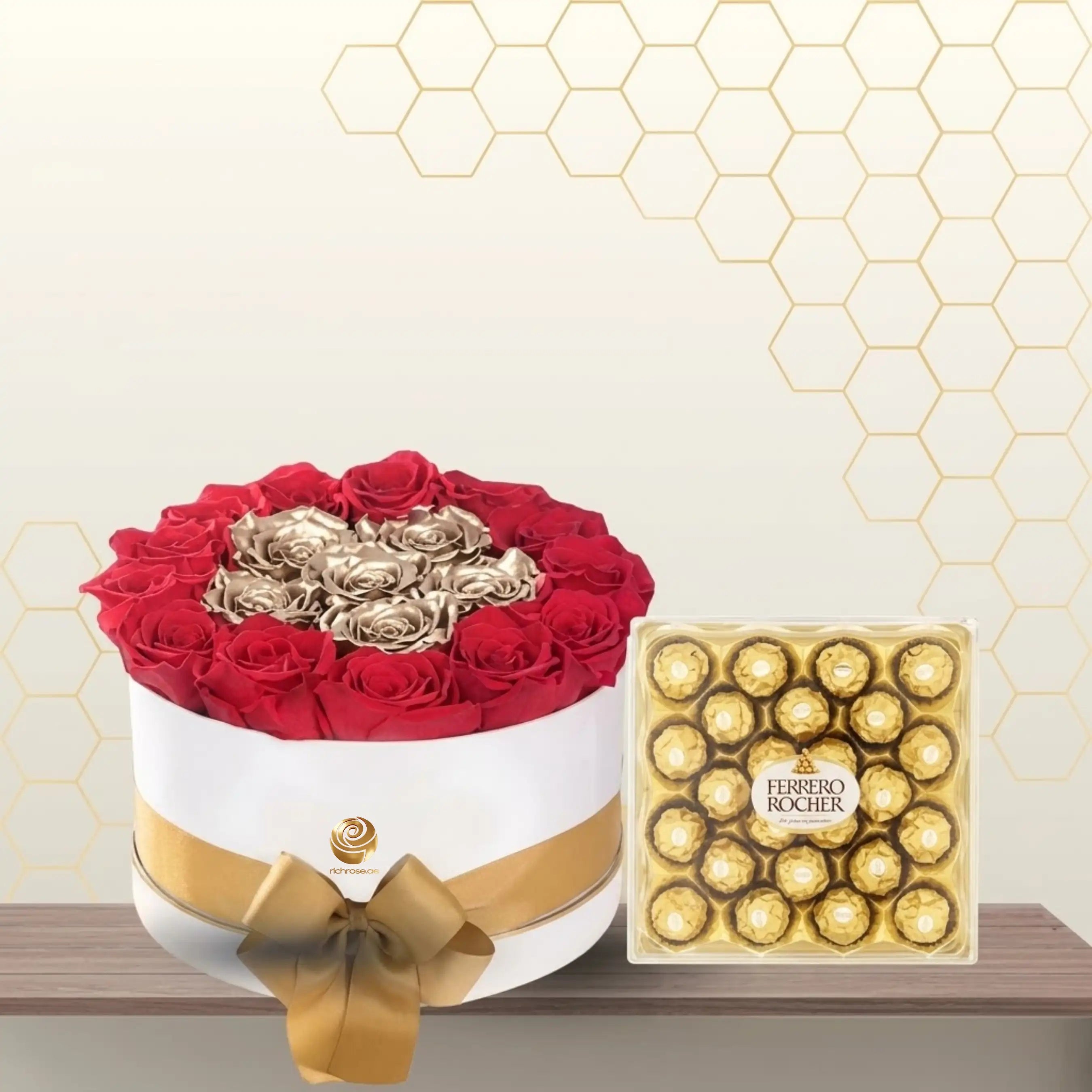 Round white flower box containing red roses surrounding gold roses, tied with a gold ribbon, next to a large box of Ferrero Rocher. Main image