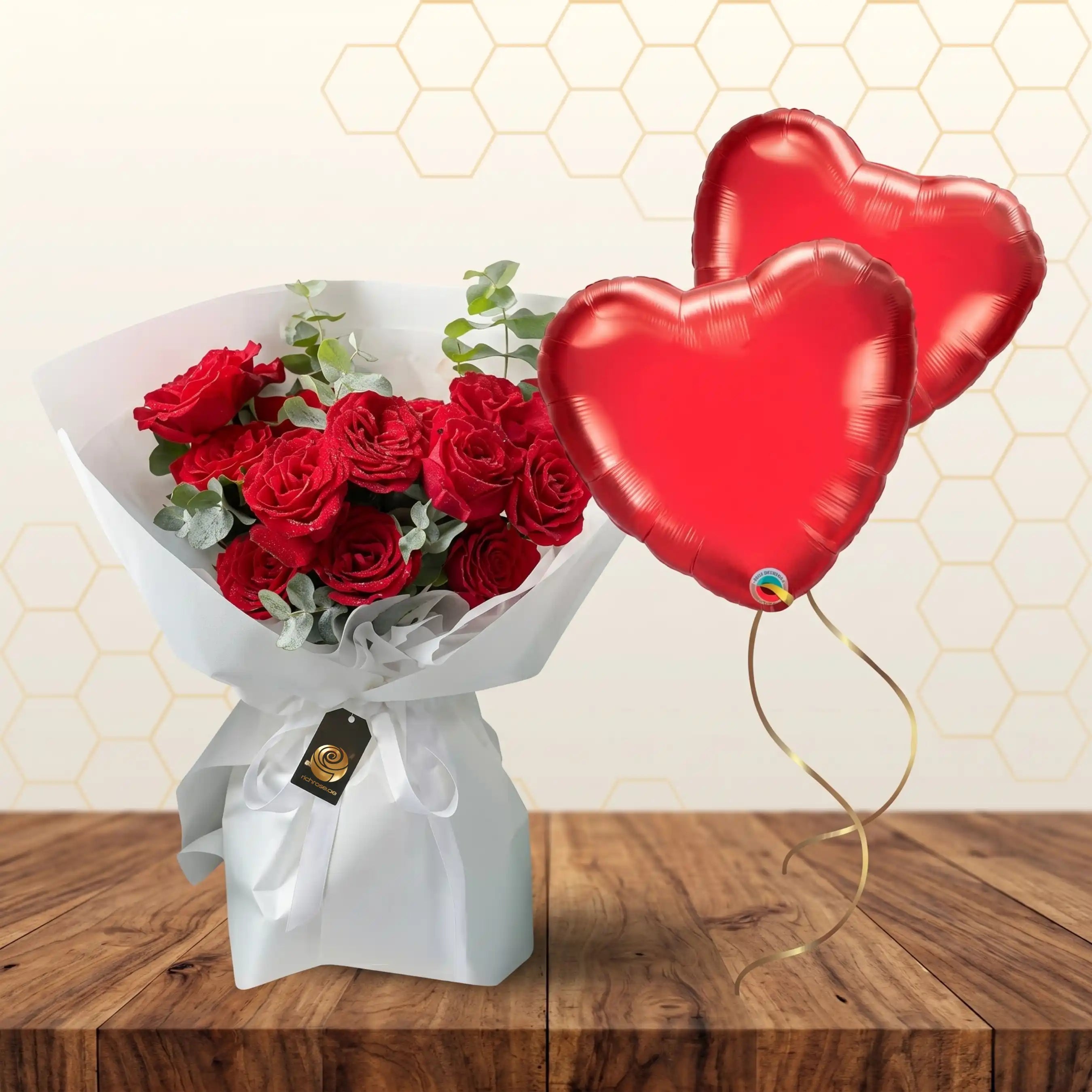 Bouquet of red roses wrapped in white paper paired with two red heart-shaped foil balloons. Main image
