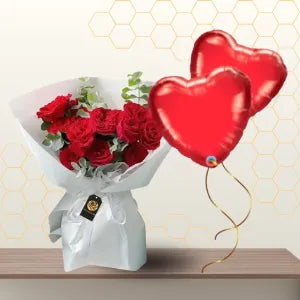 Bouquet of red roses wrapped in white paper paired with two red heart-shaped foil balloons. Main image