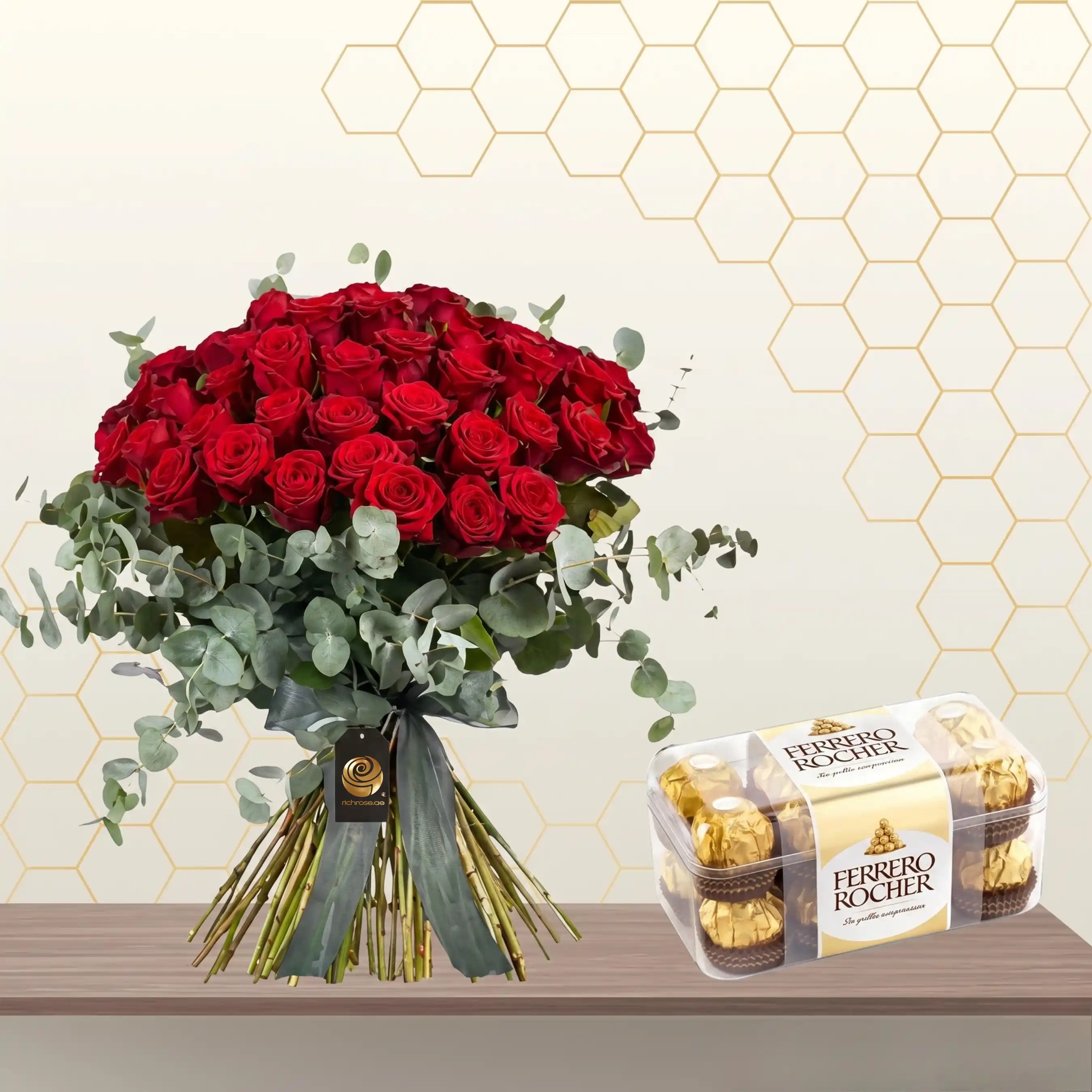 Large hand-tied bouquet of red roses and eucalyptus greenery next to a box of Ferrero Rocher chocolates. Main image