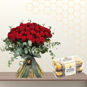 Large hand-tied bouquet of red roses and eucalyptus greenery next to a box of Ferrero Rocher chocolates. Main image