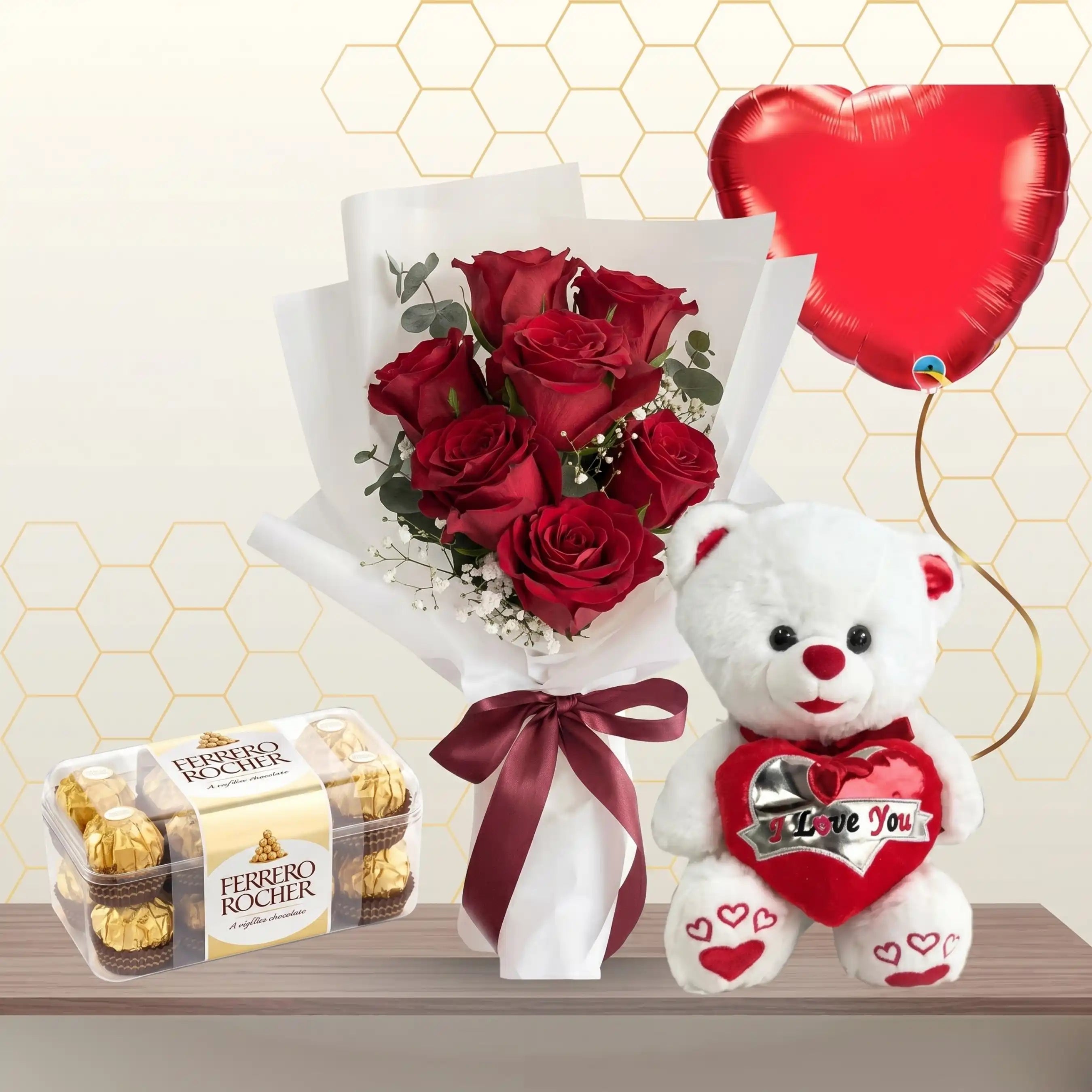 Small bouquet of three red roses in white wrapping, next to a white teddy bear, a box of chocolates, and a red heart balloon.