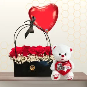 Black handbag-style flower box with red roses and baby's breath, next to a white teddy bear and a red heart balloon. Main image