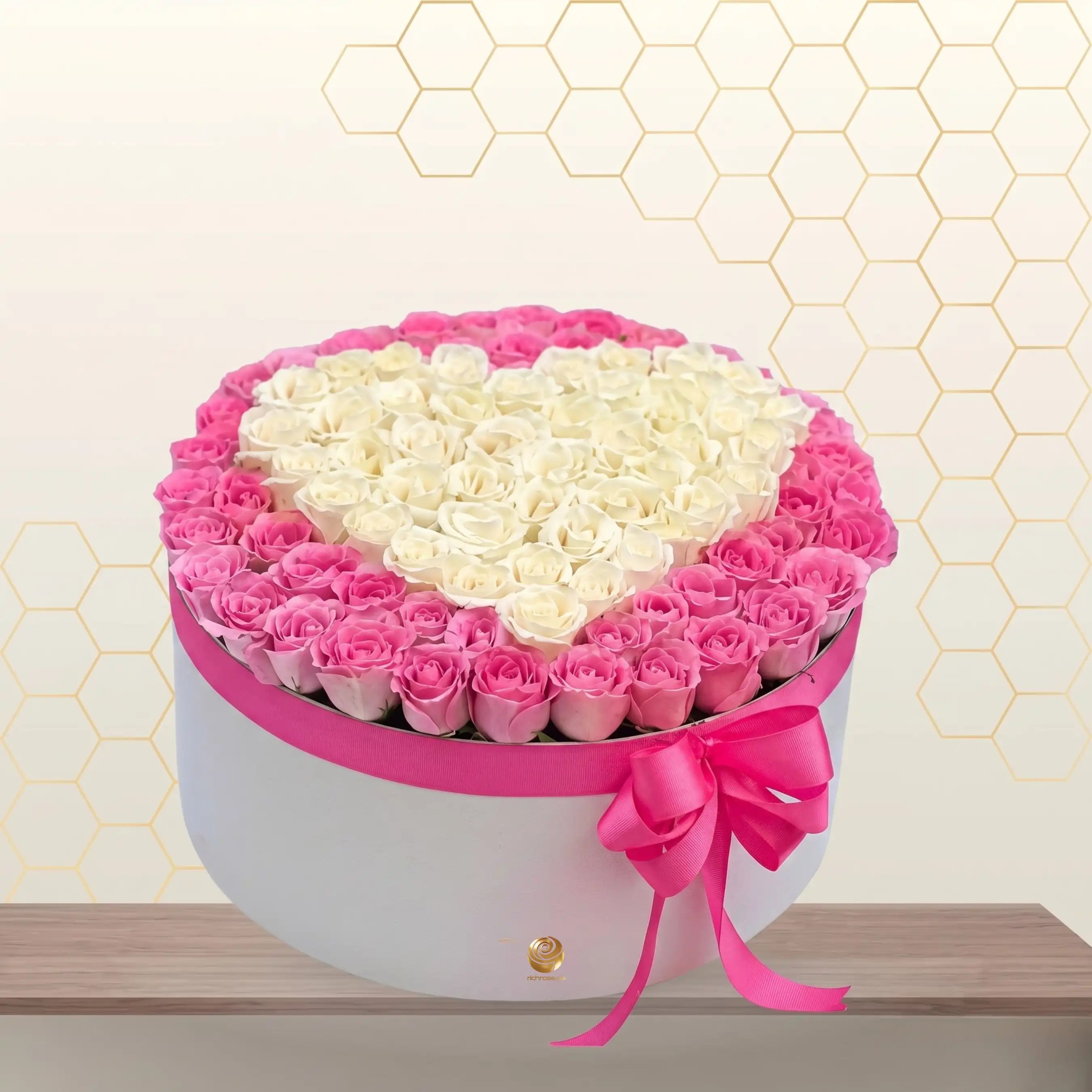 Heart-shaped arrangement of pink and white flowers in a box on a wooden surface with a honeycomb pattern in the background.
