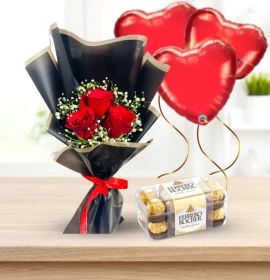 Small bouquet of red roses and baby's breath in black wrapping, next to a box of chocolates and three heart balloons.